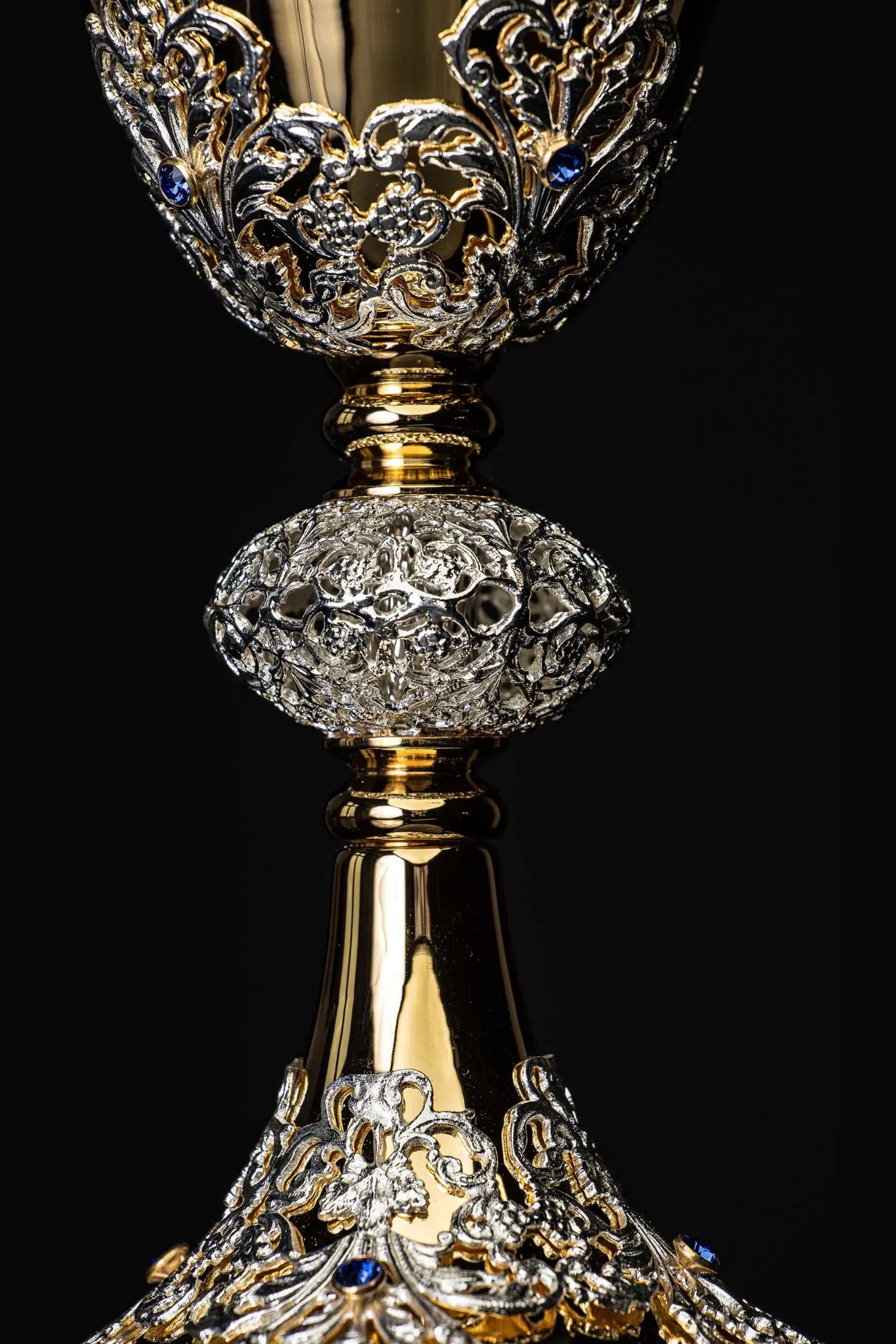 Handmade gold-plated liturgical chalice with silver-plated floral ornamentation and blue sapphire-like stones. The chalice features a decorated cup, nodus, and base.