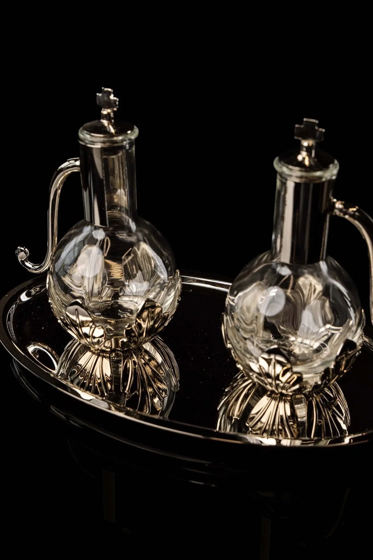 Silver liturgical cruets with cross finials and floral bases, angled view