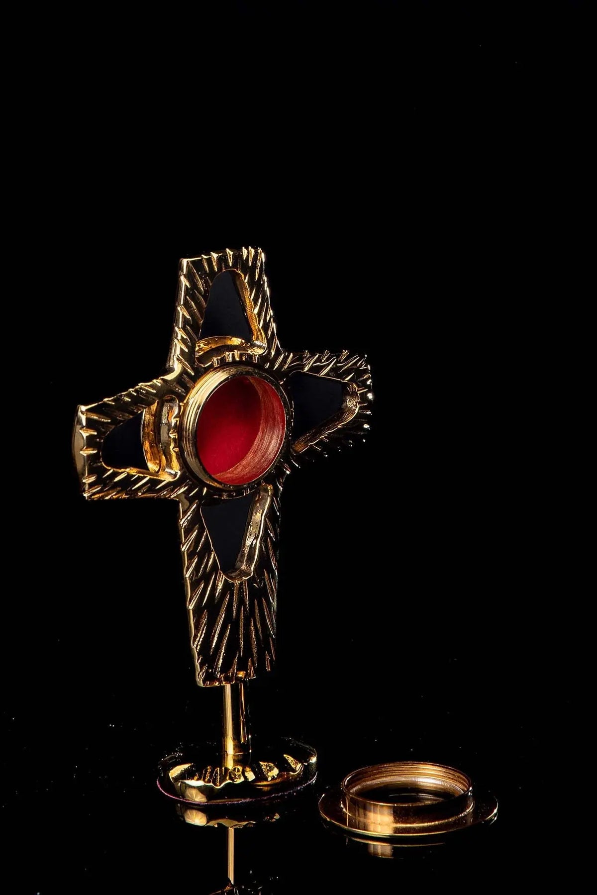 Gilded brass reliquary with cross-shaped form, angled view with red central window