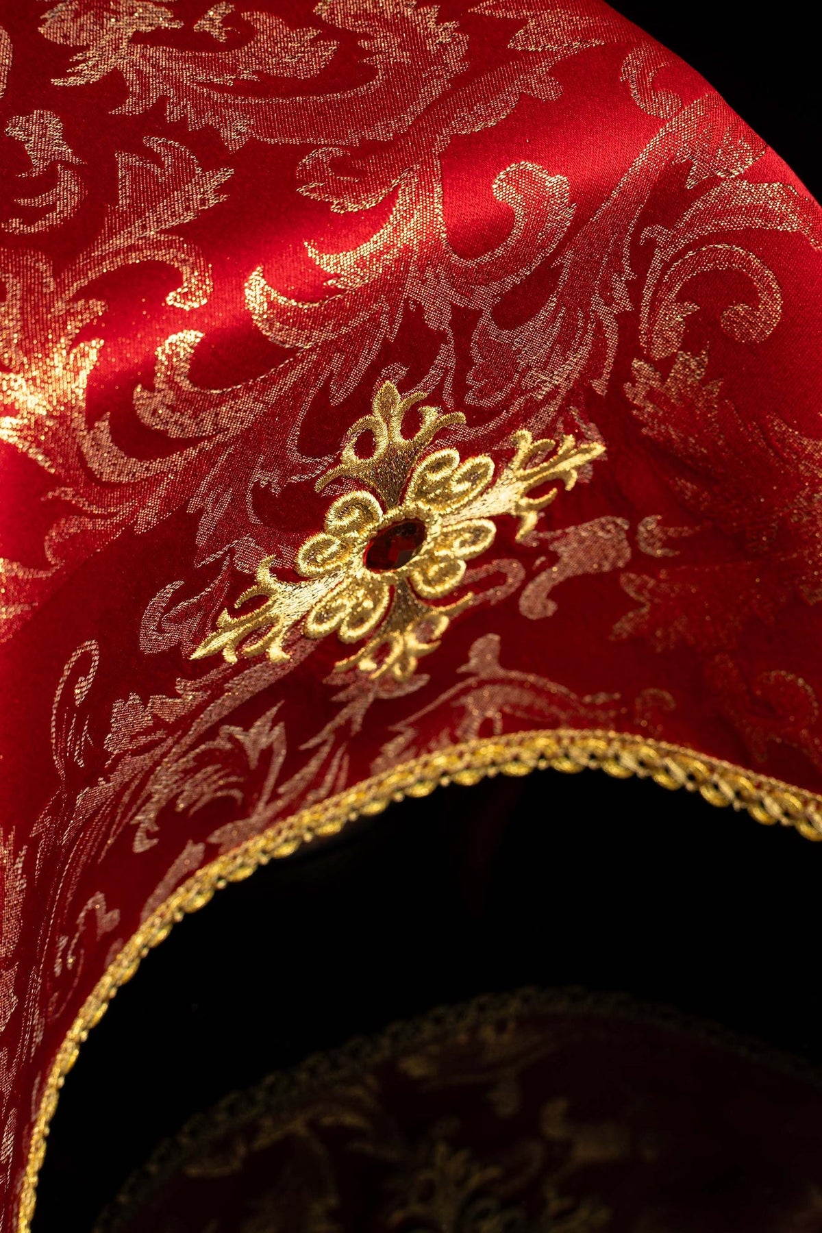 Red chalice veil with gold embroidery and scalloped trim, angled close-up