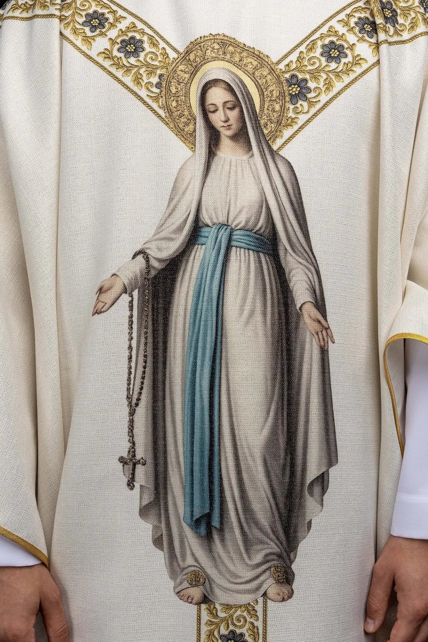Ecru chasuble with printed image of Our Lady of Lourdes, featuring a blue sash and gold floral motifs, with a matching stole.