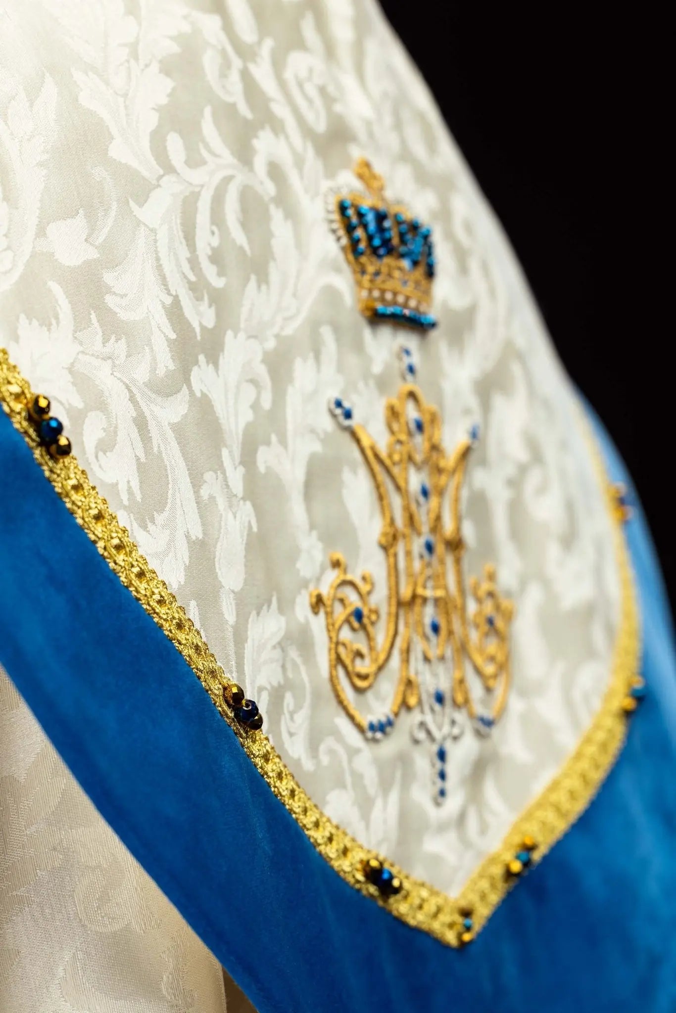 Ecru Marian cope with natural stones and blue velvet trim, part of the Handmade Collection, featuring an ornate metal clasp and gold tassel.