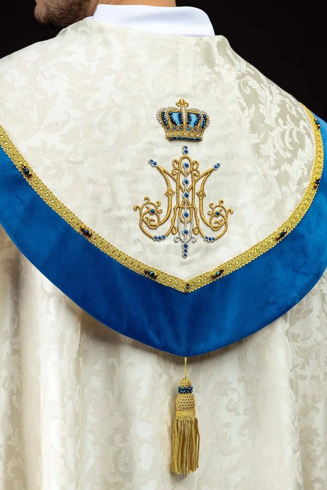 Ecru Marian cope with natural stones and blue velvet trim, part of the Handmade Collection, featuring an ornate metal clasp and gold tassel.