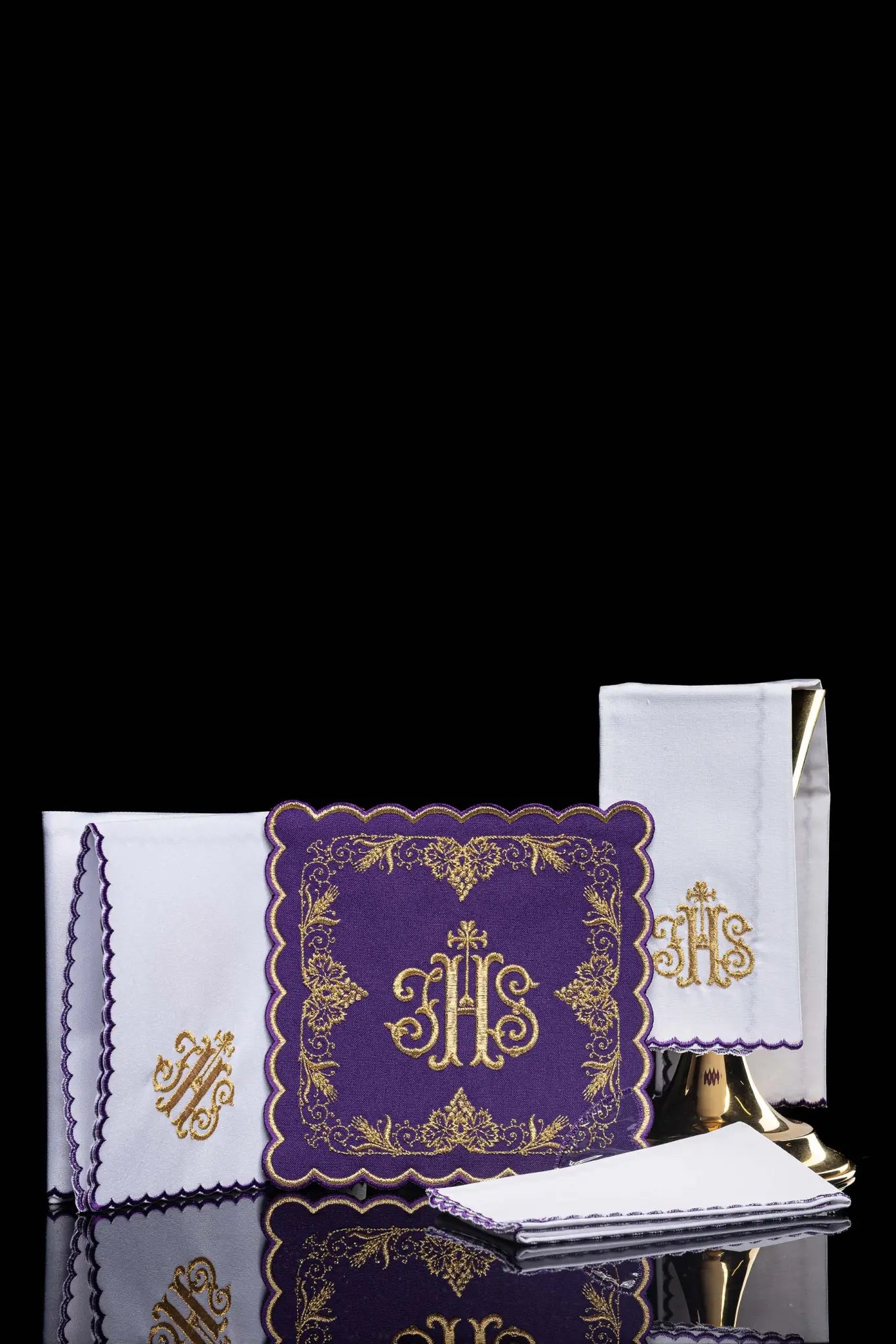 Purple chalice linen set with gold IHS embroidery, vine leaves, and wheat sheaves. Includes a purple pall, white corporal with IHS, and white purificator and lavabo towel with gold crosses and purple scalloped edges.
