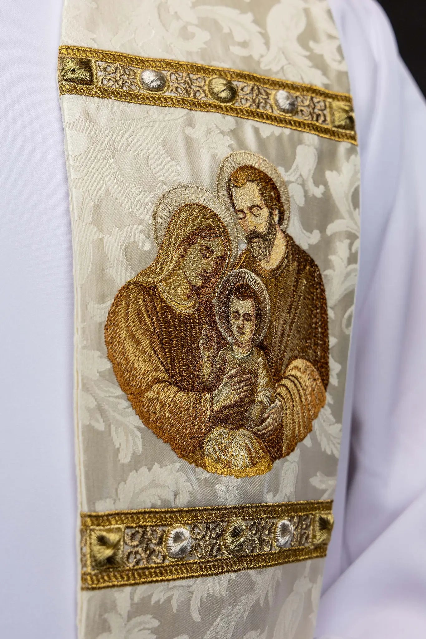Ecru stole with Holy Family image on one side and IHS monogram on the other, featuring gold trim and tassels.