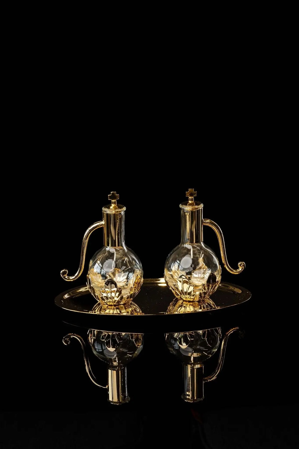Gold liturgical cruets with floral accents and cross lids on tray, front view