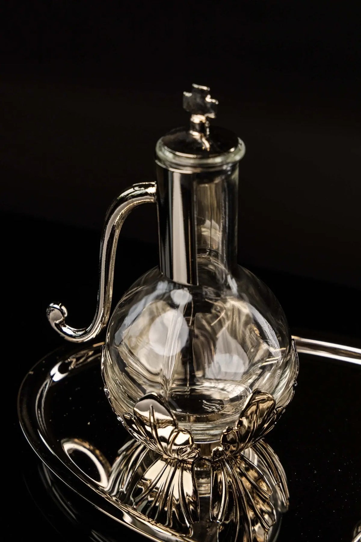 Silver liturgical cruet with floral base and curved handle, close-up