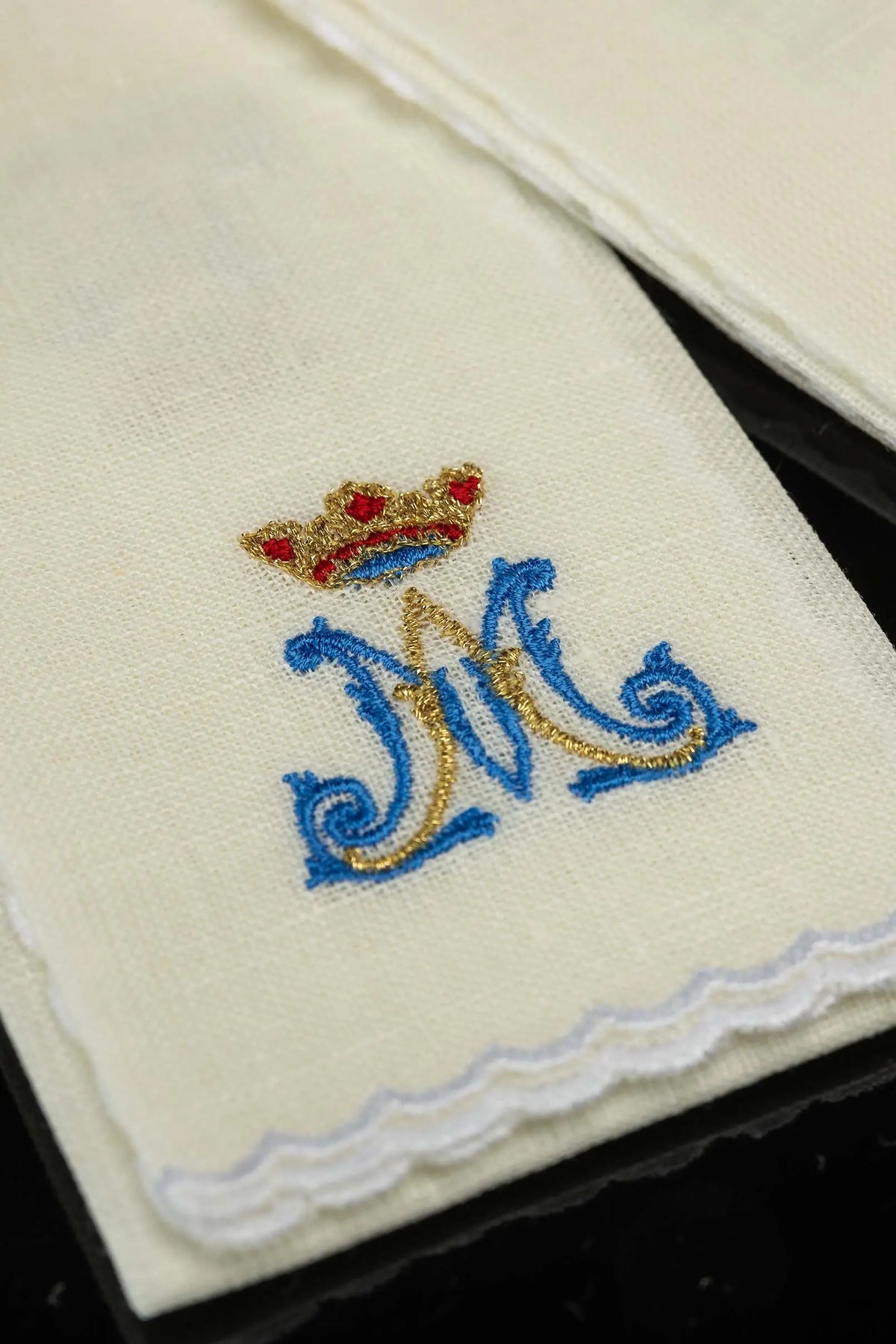 Ecru linen purificator with crowned Marian monogram and scalloped edge, close-up view
