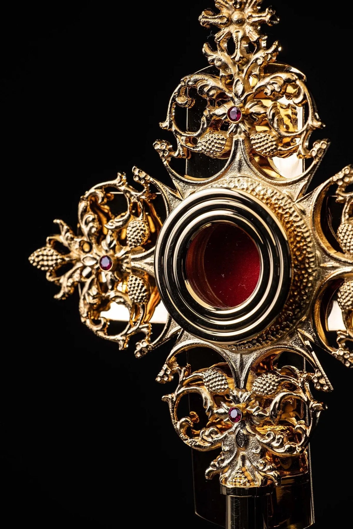 Gilded brass reliquary with red center and raised floral details, angled close-up