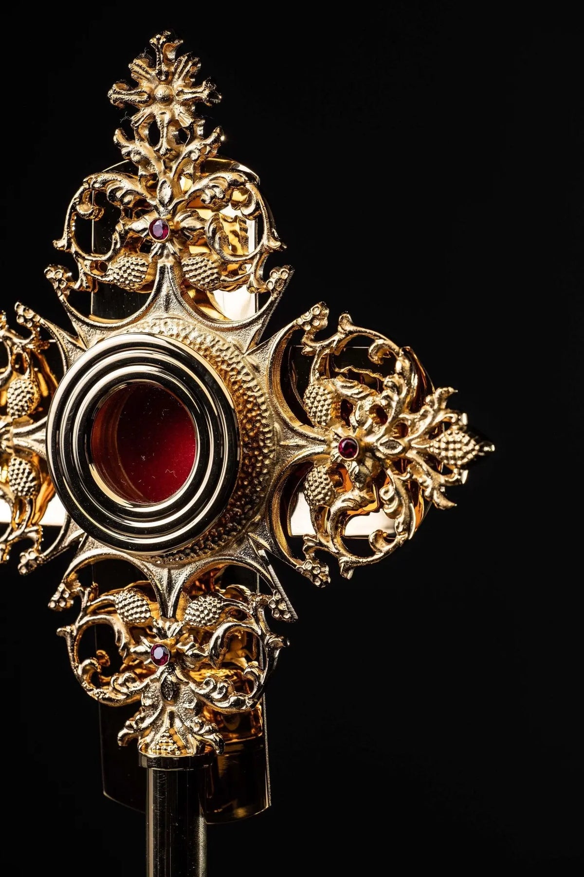 Gilded brass reliquary with red center and ornate floral motifs, side close-up