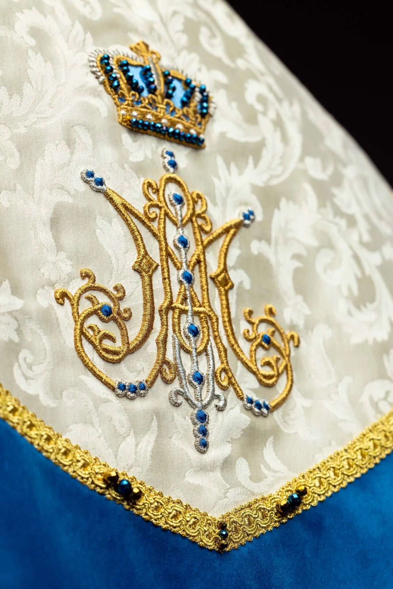 Ecru Marian cope with natural stones and blue velvet trim, part of the Handmade Collection, featuring an ornate metal clasp and gold tassel.